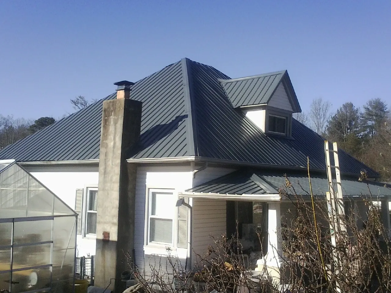 Dark blue standing seam metal roof on a white farmhouse with dormer — Slate & Tile Roof Repair by Roofing Brothers in Addison