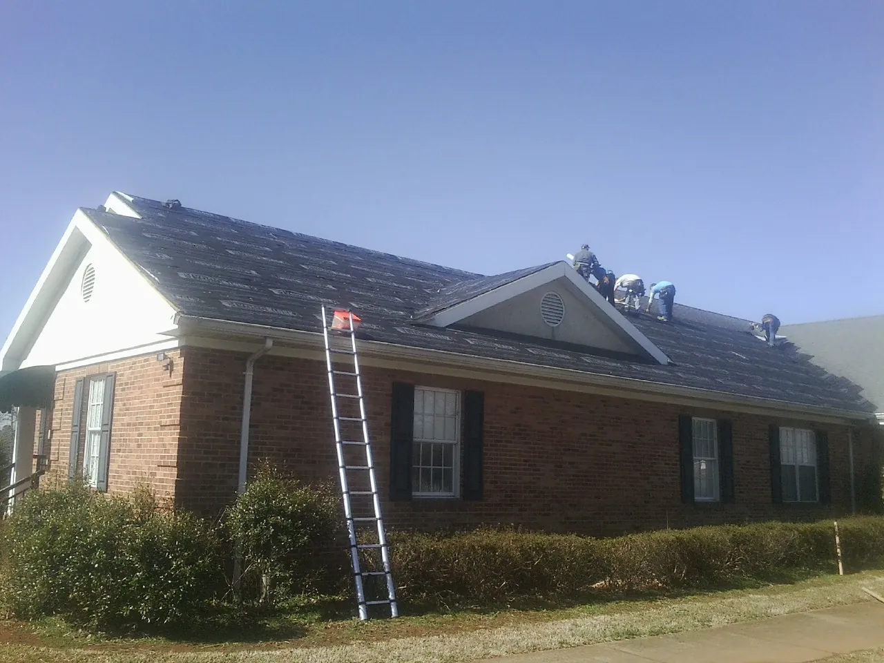 Crew tearing shingles off a brick ranch roof with a ladder set — Metal Roof Repair work by our crew in Addison