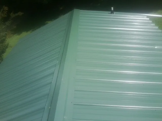 New green metal panels meeting at the ridge of a roof — Flat Roof Repair work by our crew in Addison