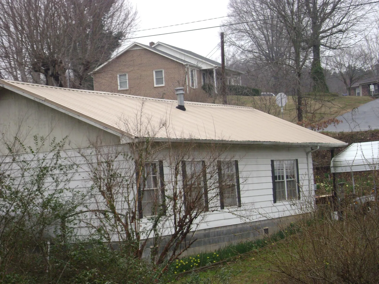 Tan metal roof on a white sided house set into a hillside — Commercial Roofing by Roofing Brothers in Addison